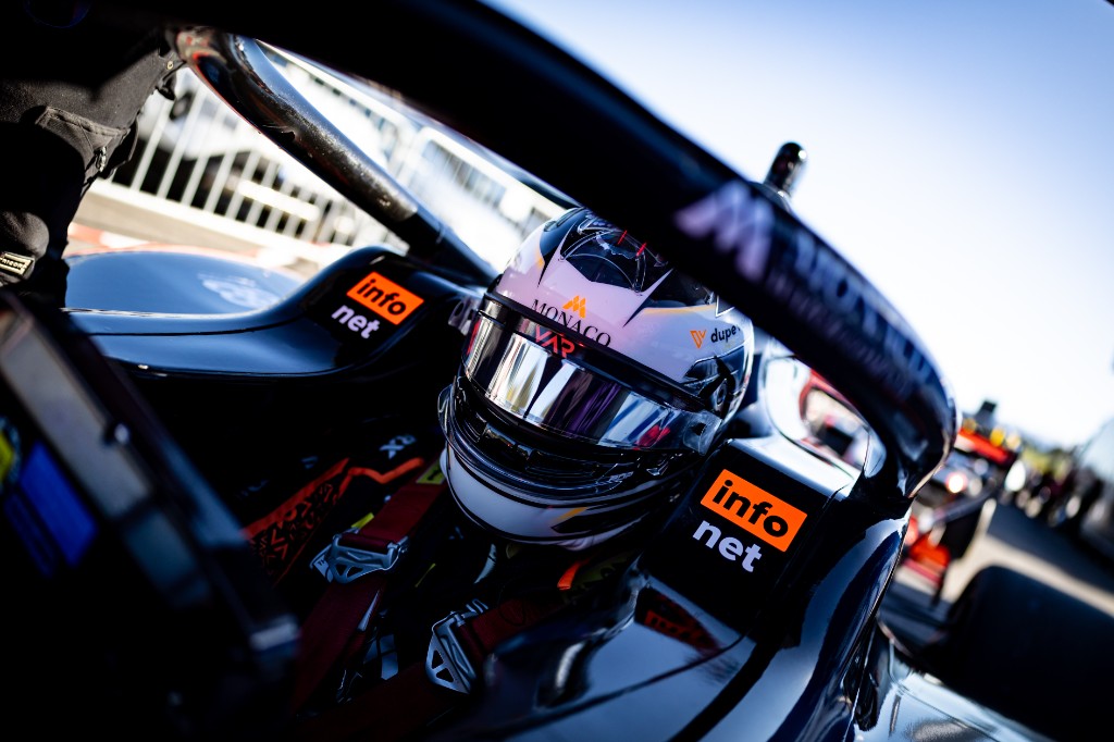 Close-up of Andrea Dupé in the cockpit — helmet and Infonet sponsors